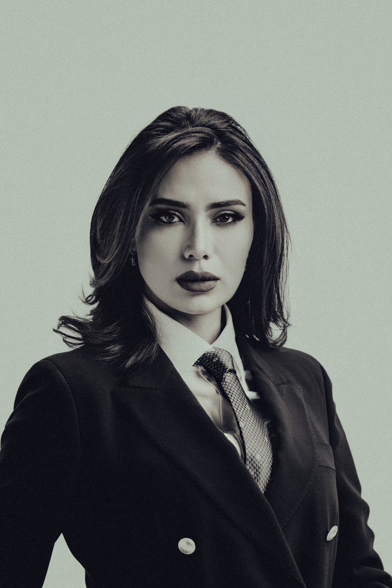 Corporate portrait of a woman in a black blazer, white shirt, and tie against a neutral studio backdrop