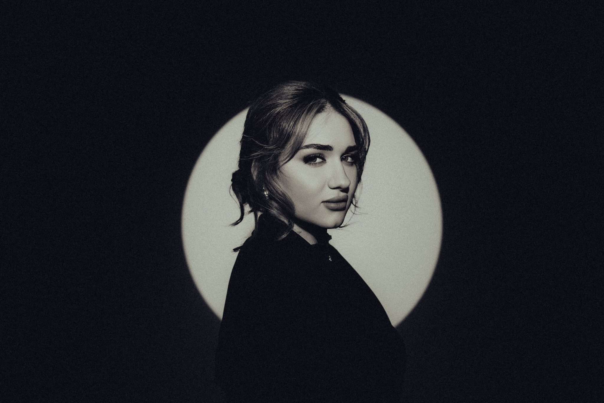 Moody corporate portrait of a woman in a black coat lit by a circular spotlight against a dark background