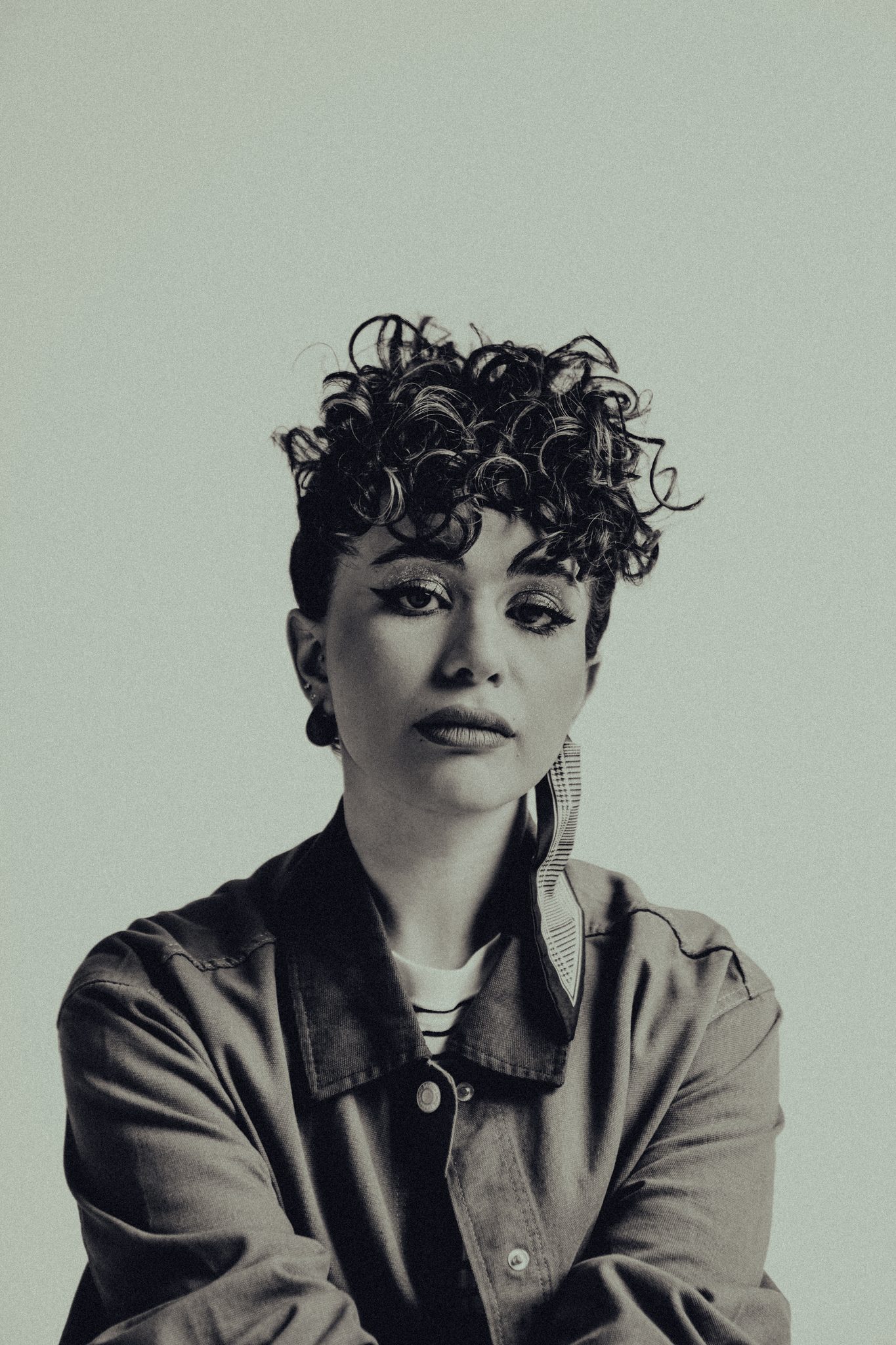 Black-and-white executive portrait of a woman with curly hair and a statement earring, arms crossed