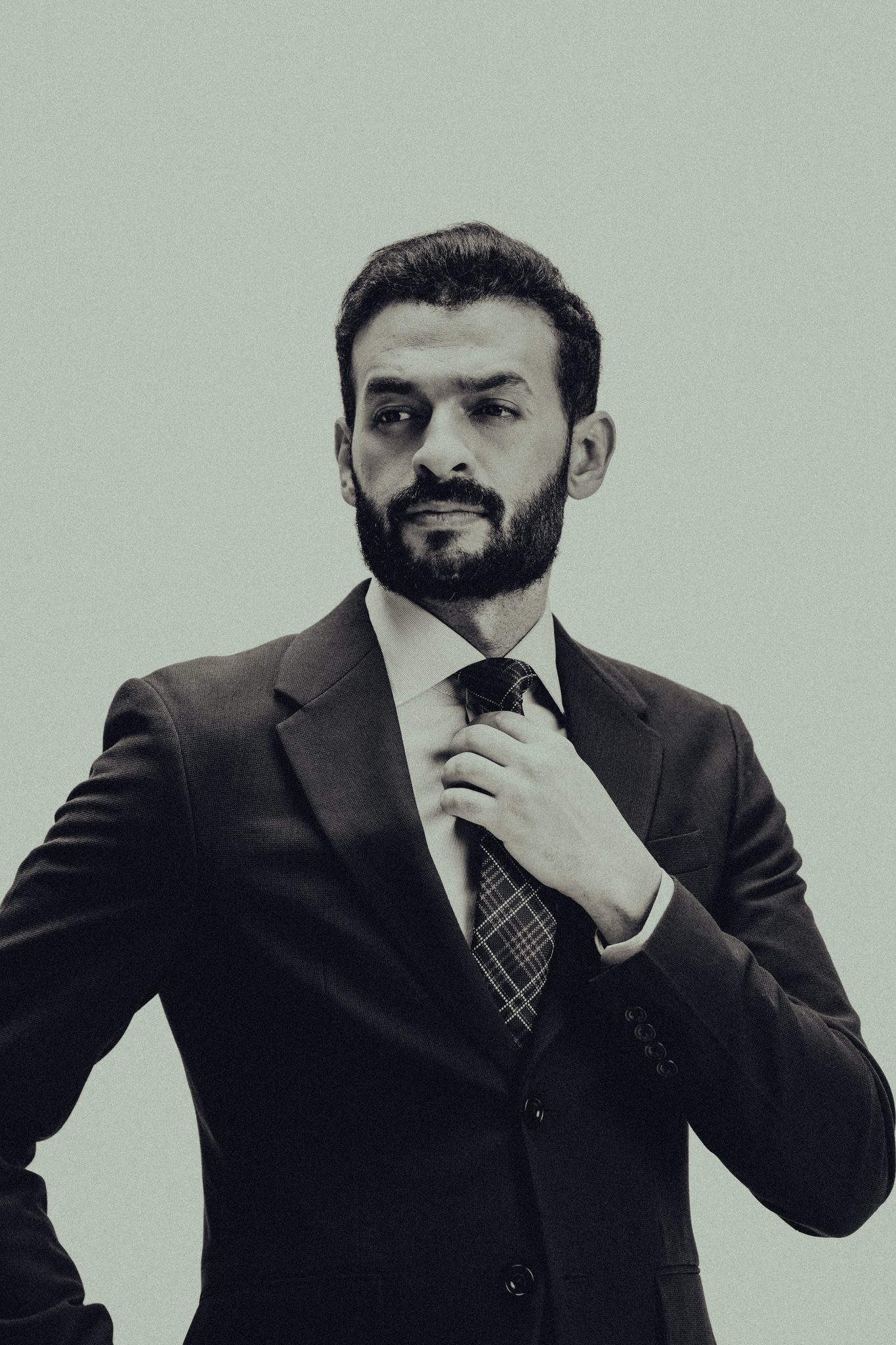 Black-and-white executive portrait of a bearded man in a suit adjusting his tie